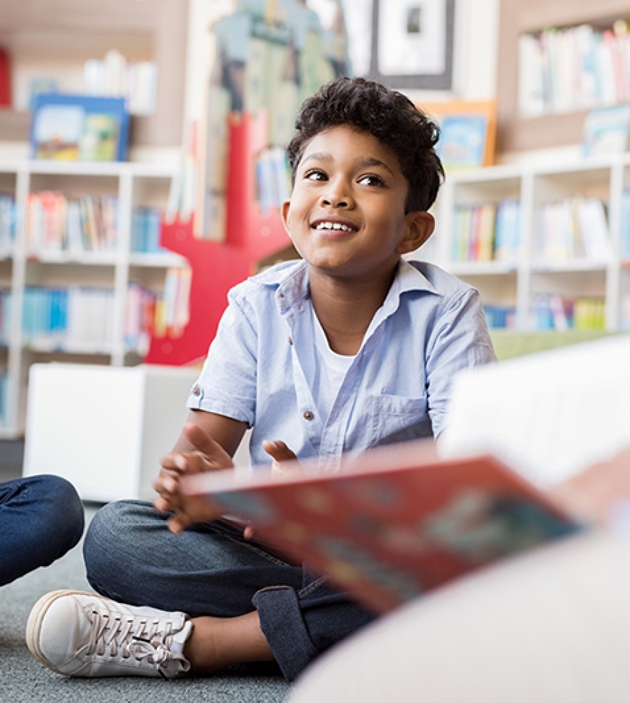 Multiethnic group of kids sitting on floor in circle around the teacher and listening a story. Discussion group of multiethnic children in library talking to woman. Portrait of smiling hispanic boy in elementary school.