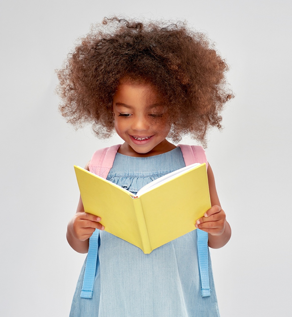 childhood, school and education concept - happy little african american girl with backpack reading book over grey background